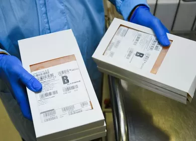 a lab worker is wearing a blue gown and gloves and is holding two boxes of blood packs marked B positive