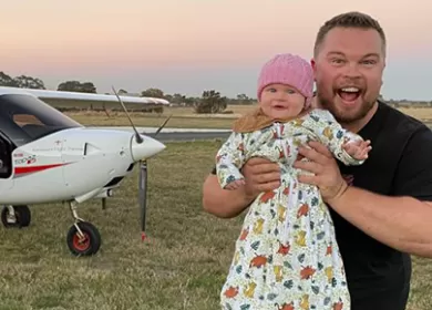 man holding a baby smiling at camera in front of an airplane