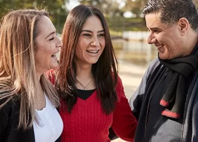 photo of two women and a man standing outdoors having a conversation and smiling