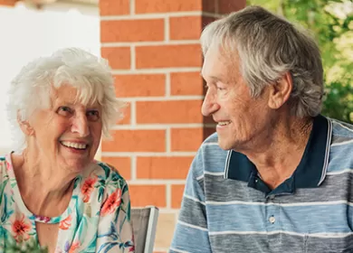 photo of an older couple seated at a table outside laughing and smiling