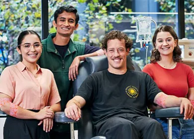 a group of people smiling to camera, one is seated in a donor chair