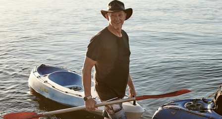 Man carrying paddle in front of kayak floating on water