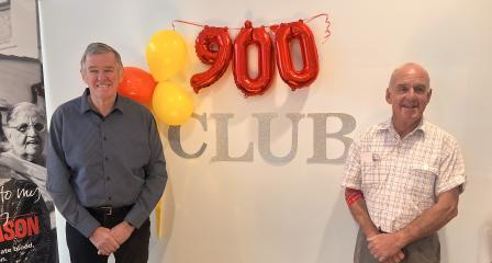 two men standing either side of a sign that reads 900 Club