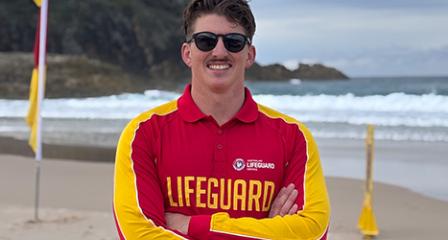 Image of a young male in his 30s working as a lifeguard with the ocean behind him