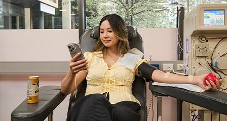 Image of a young female donating blood while looking at her phone