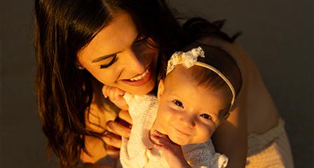 image of a woman holding her baby girl and smiling as the golden sunset shines on their faces