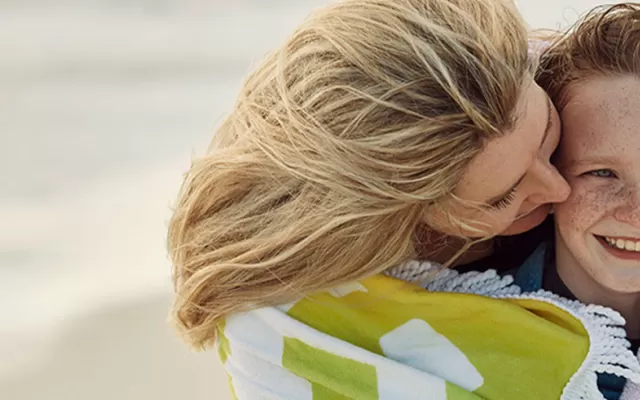 a mother and child on a beach smiling with a beach towel over their shoulders