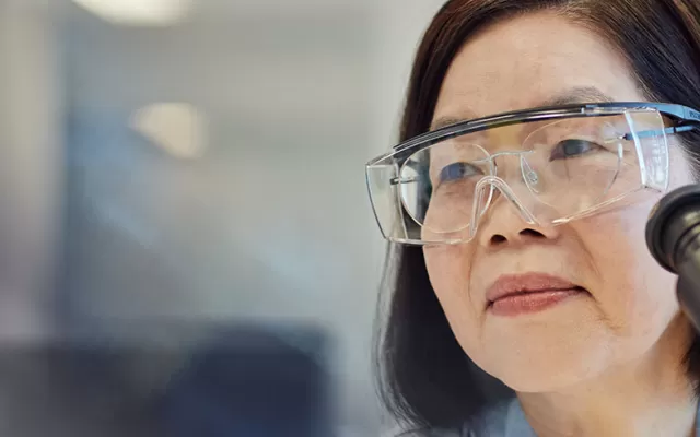 a scientist wearing goggles is looking up from a microscope