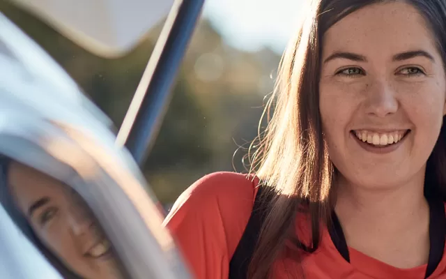 close up of a young woman next to a car smiling with sun shining