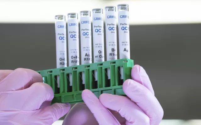 Pair of pink gloved hands holding test tubes for blood testing