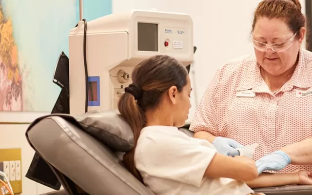 Blood donor Phoebe with a nurse assisting her as she gives blood