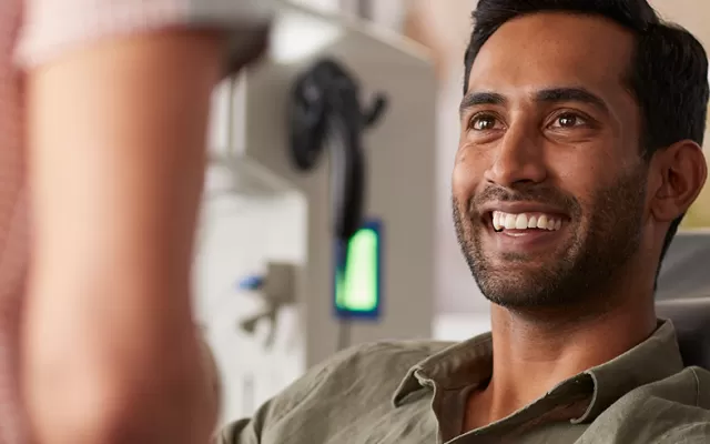 a male donor is sitting in a donation chair and smiling, a nurse is in the foreground