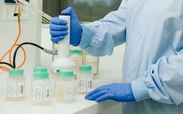 a scientist dressed in a blue gown and blue gloves is using a machine to pipette milk into jars