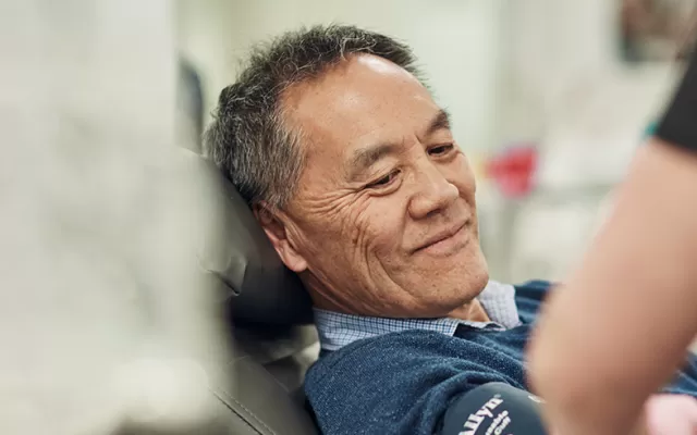 a donor is seated in a donation chair smiling at a staff member in the foreground