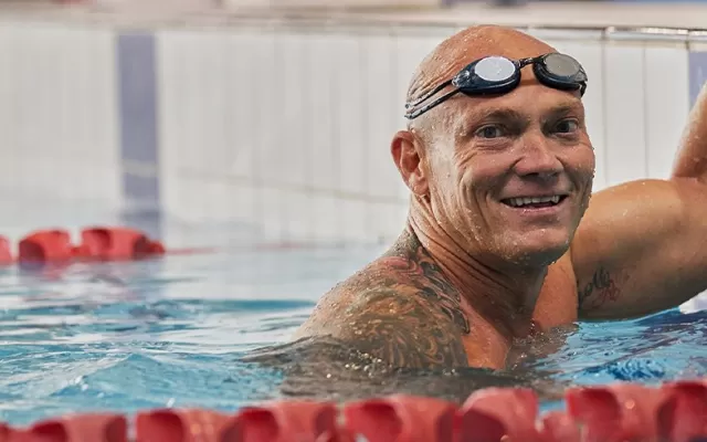 photo of michael klim at the end of a swimming lane, he is wearing goggles on his forehead and smiling at the camera
