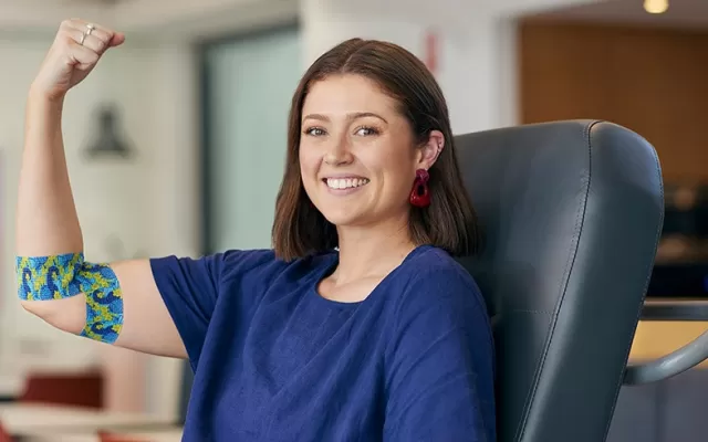 photo of a woman seated in a donor chair smiling and holding out her arm