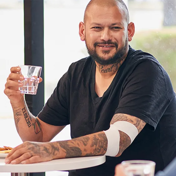 a man seated at a table smiling with a bandage around his elbow