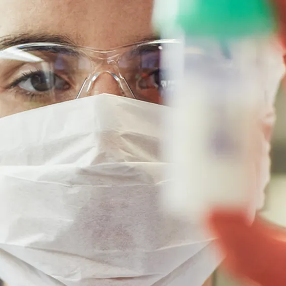 a scientist is wearing a facemask and a hairnet and is holding up a milk sample jar