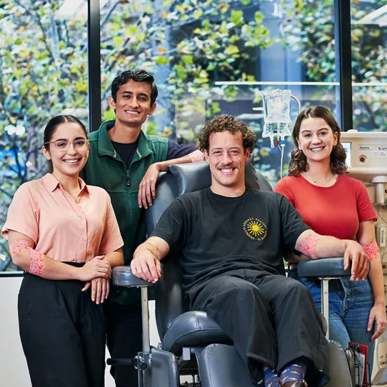 a group of people smiling to camera, one is seated in a donor chair