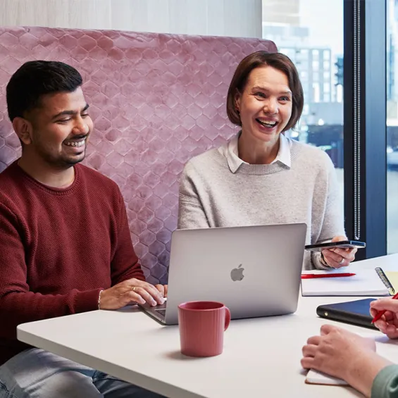 three people seated at a table in an office chatting and smiling