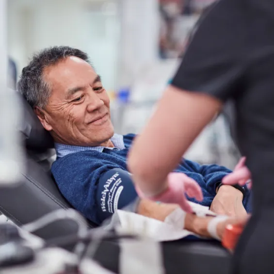 a person seated in a donor chair while a nurse prepares to begin the donation