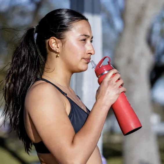 a woman drinking from a reusable water bottle while outdoors