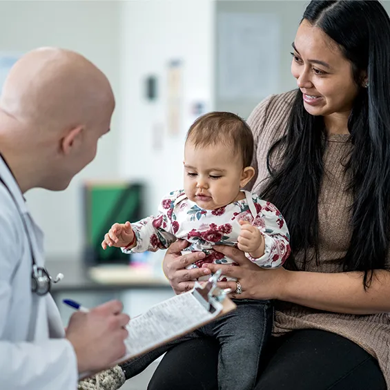 Image of doctor in white coat talking to mother holding a baby