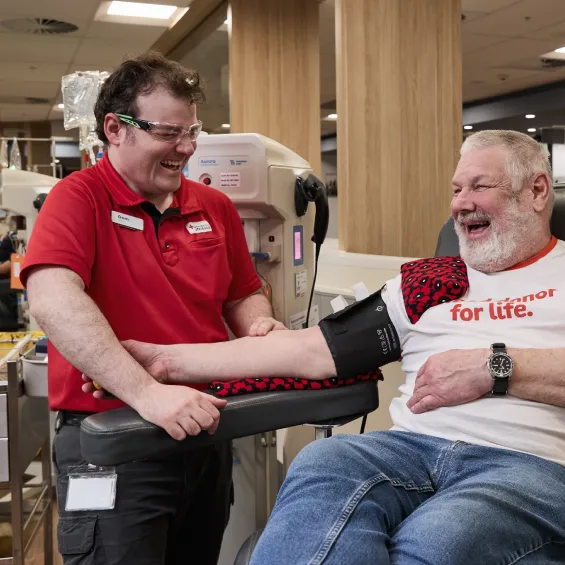 A staff member getting a man ready for his donation on the couch. They are both laughing.