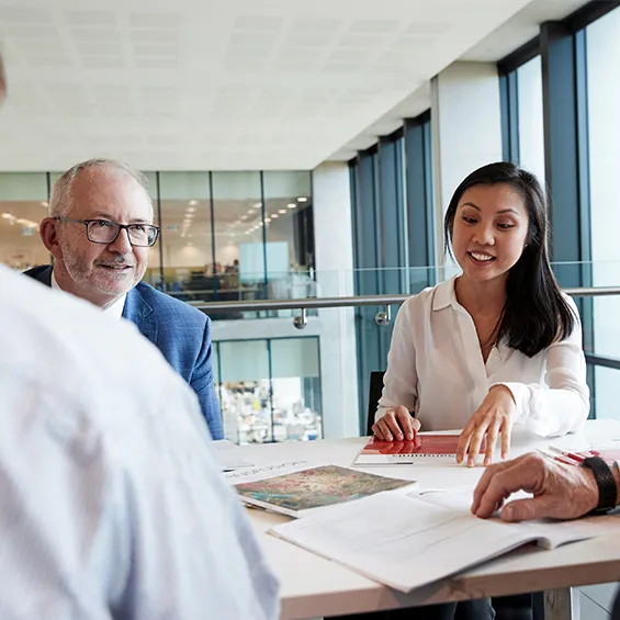 three people seated at a table in an office chatting and smiling