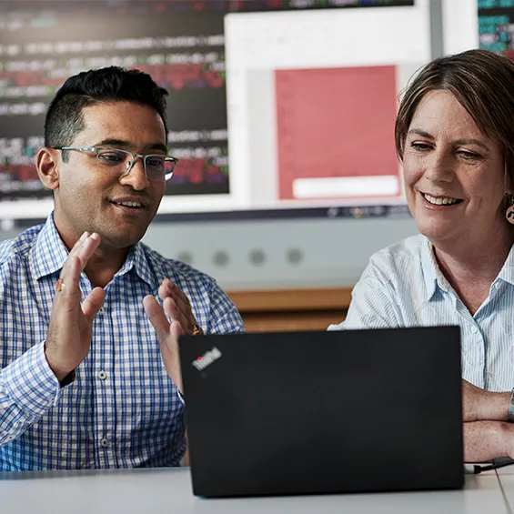 two people talking at a desk with a laptop