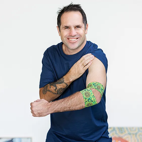 photo of artist brad hore smiling and pulling up his sleeve to show the bandage he designed around his elbow