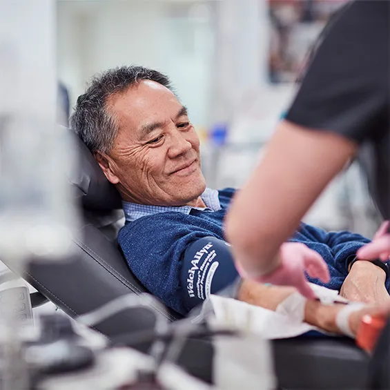 a person seated in a donor chair while a nurse prepares to begin the donation