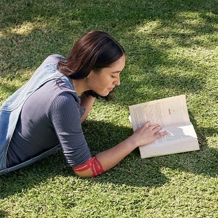 a woman lying on grass reading a book with a bandage around her elbow