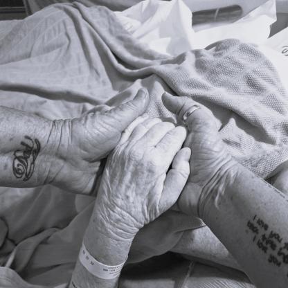 A photo of 3 arms with hands together over a hospital bed