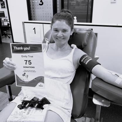 Emily donating on a couch holding up a 75 Donation milestone card