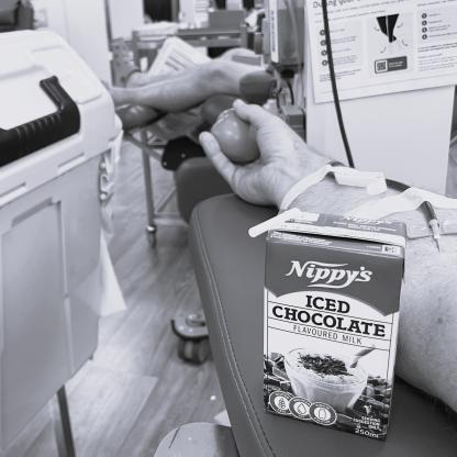 An arm with a needle during a donation and a box of nippys Iced coffee 