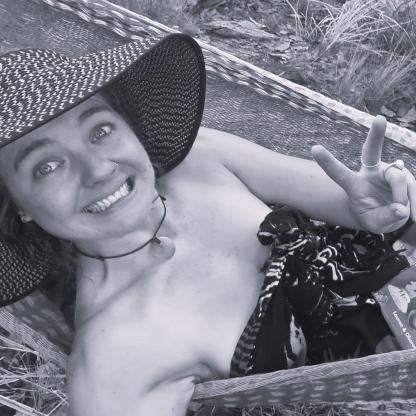 A woman in a sarong and a beach hat in a hammock smiling