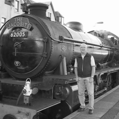 man smiling to camera standing in front of an old steam train