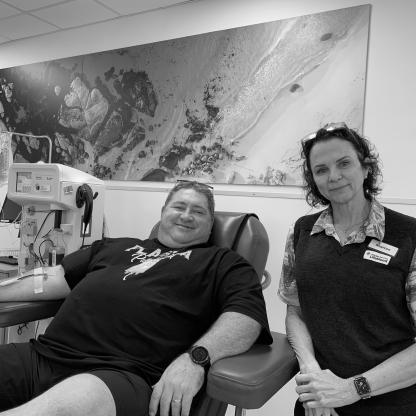man smiling to camera during his donation with a Lifeblood staff member by his chair
