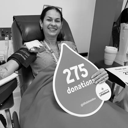 woman sitting in a donor chair holding a 275 donations sign