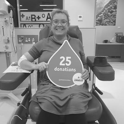 woman sitting in a donor chair holding a 25 donations sign