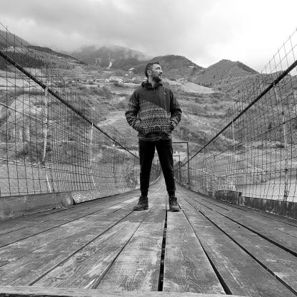 man standing on a wooden bridge staring out to the river it crosses