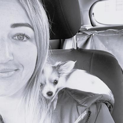 A woman taking a selfie in a car with a small dog on her shoulder