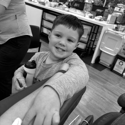 young boy holding a piece of cotton wool over where a needle was removed from the arm after a donation