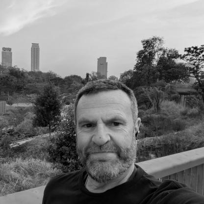 man taking a selfie with trees and a city scape in the background