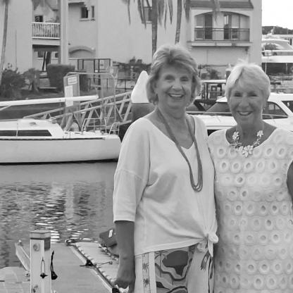 2 woman standing on a jetty, with boats in the background on the river, smiling to camera