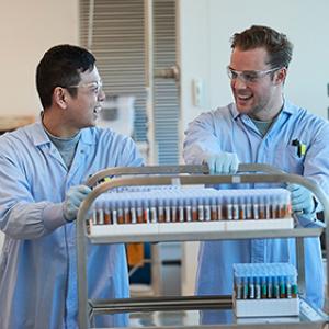 Two male laboratory technicians pushing trolley of blood samples