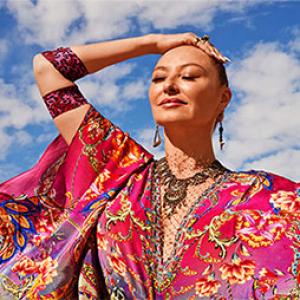 photo of camilla franks with a sky backdrop, she is wearing a pink patterned dress and has the bandage she designed around her right elbow