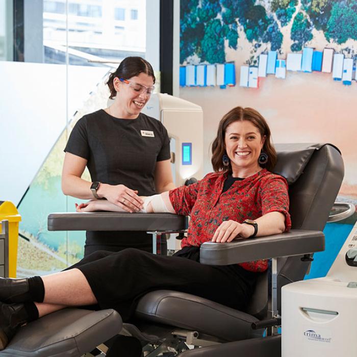 a donor is seated in a chair and smiling while a nurse prepares the donation