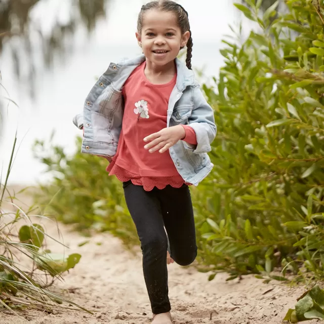 a child is jogging on sand alongside some trees, the sea is in the background